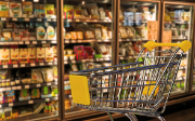 Empty shopping trolley in front of a full supermarket refrigerated shelf.